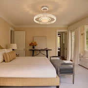 Modern ceiling fan with lights installed in a bright bedroom with neutral decor and warm crystal ring illumination.