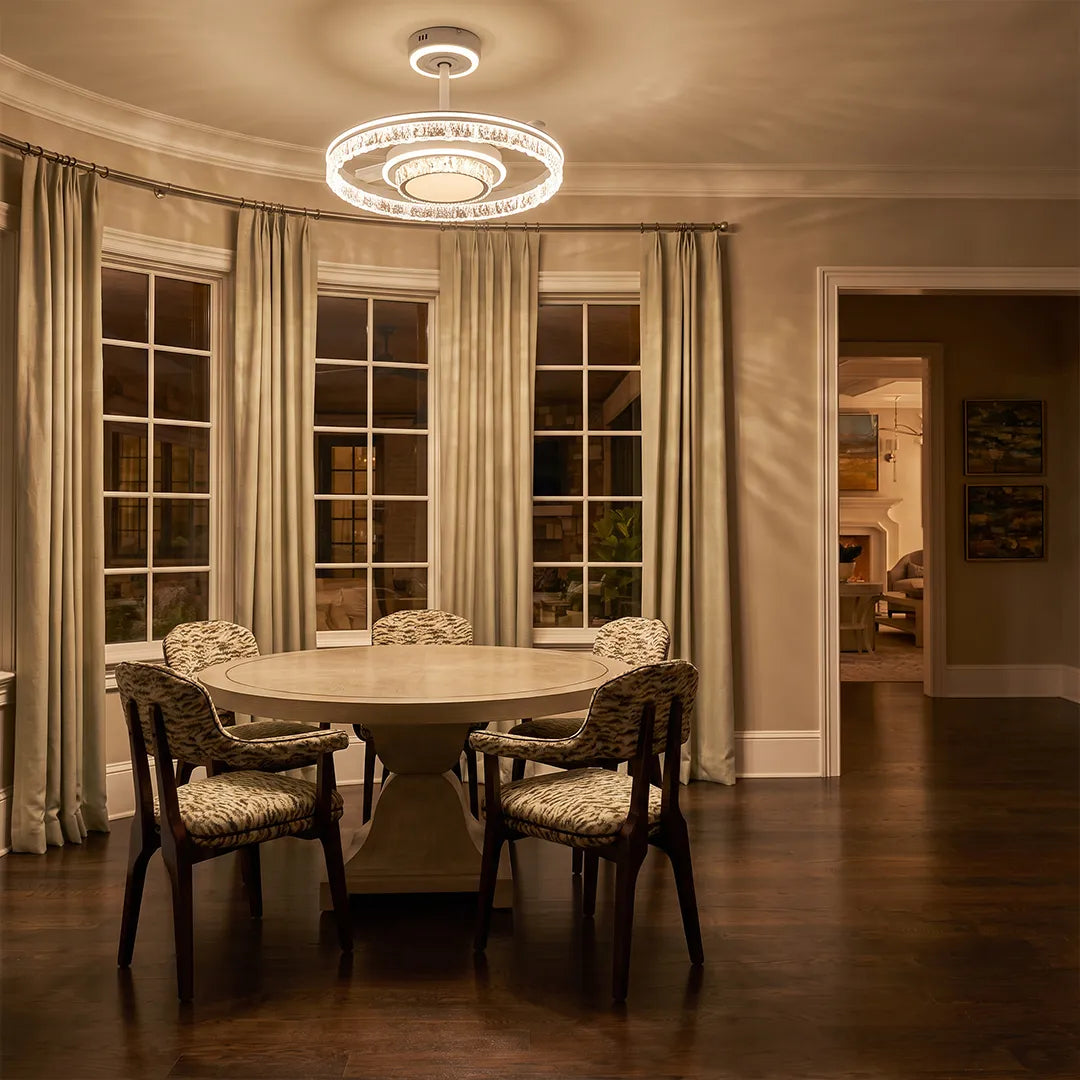 Modern ceiling fan with lights displayed over a dining area with round table and elegant crystal ring design.