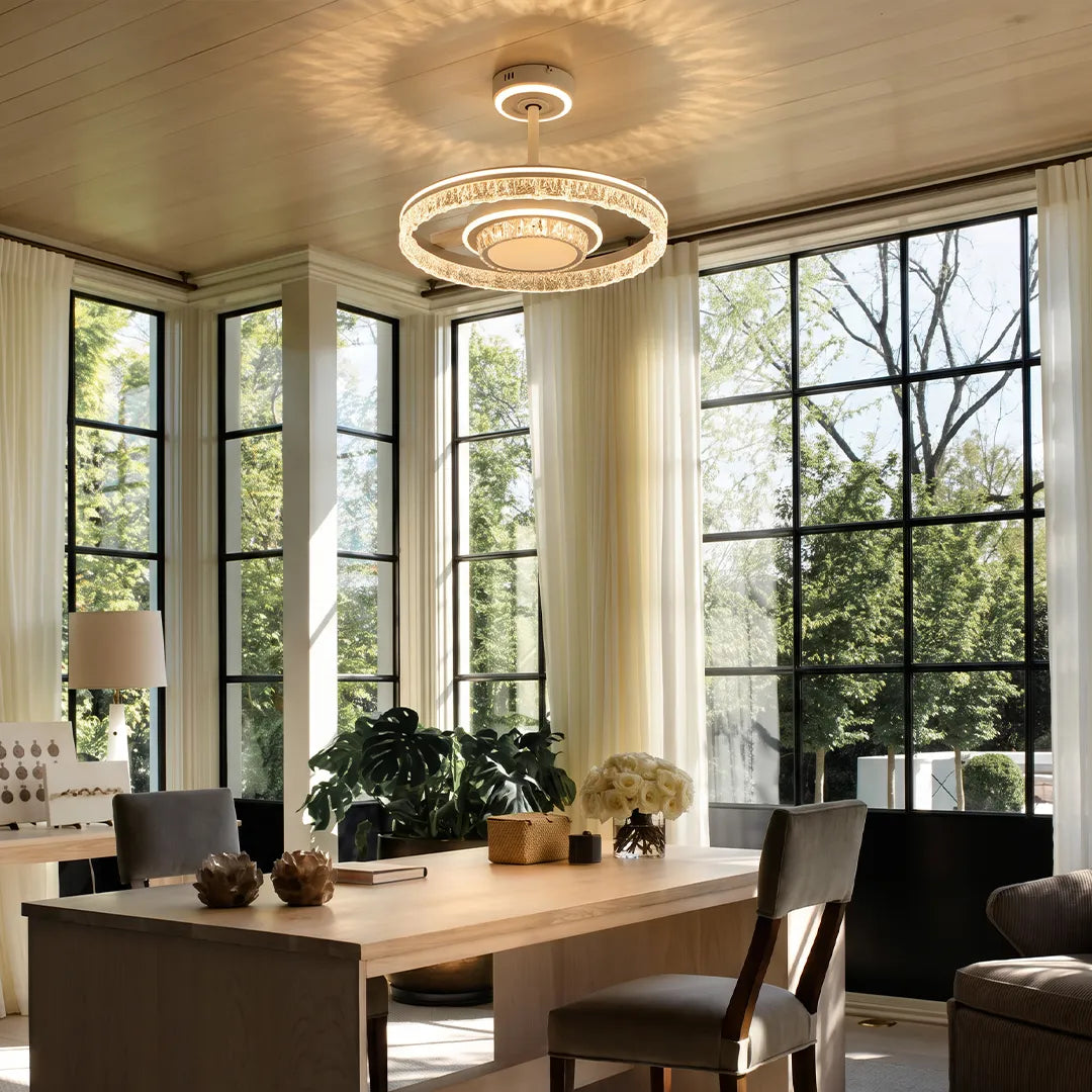 Modern ceiling fan with lights installed in a sunlit home office with tall windows and crystal ring detailing.