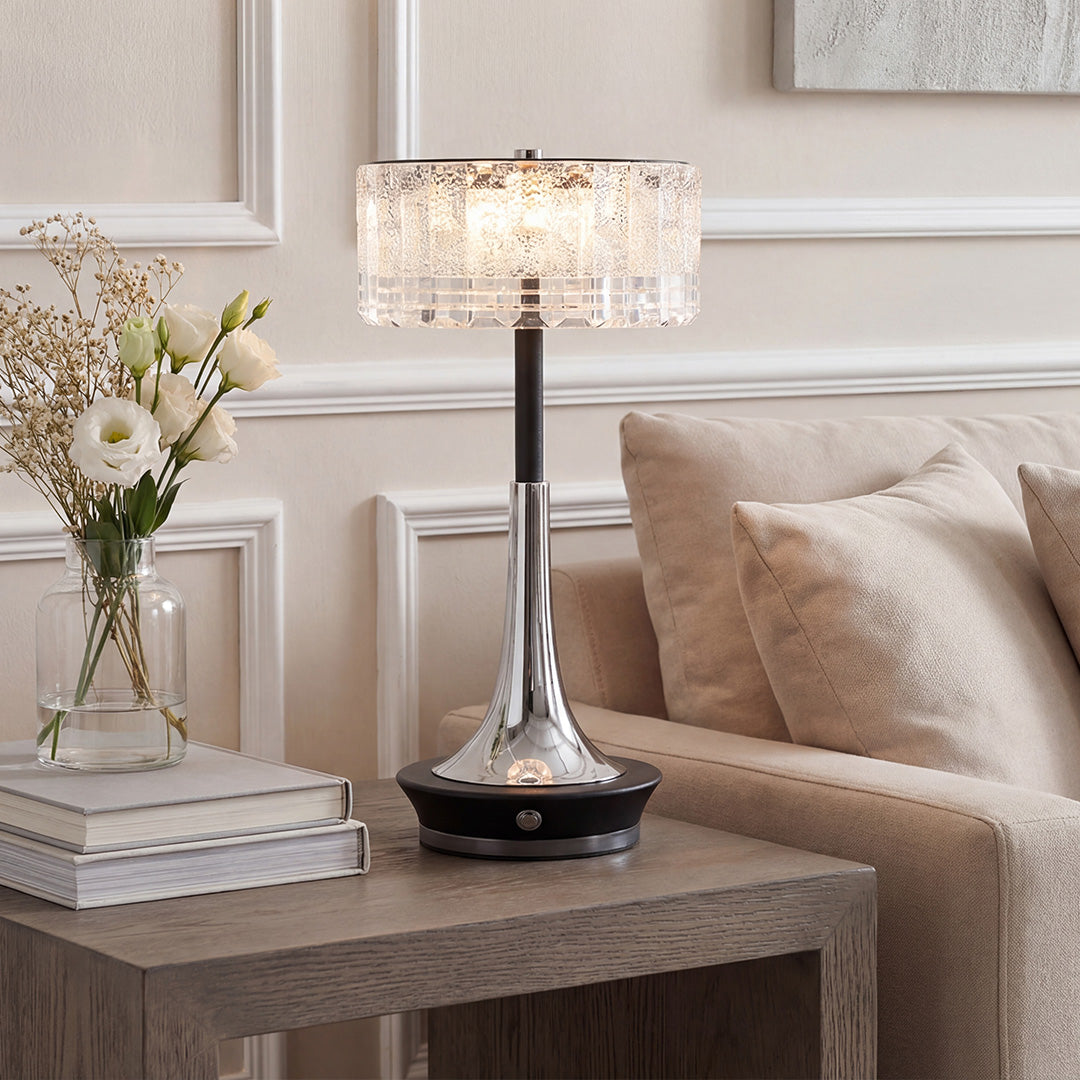 Modern chrome and black table lamp with a crystal shade on a modern wood table beside a sofa.