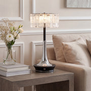 Modern chrome and black table lamp with a crystal shade on a modern wood table beside a sofa.