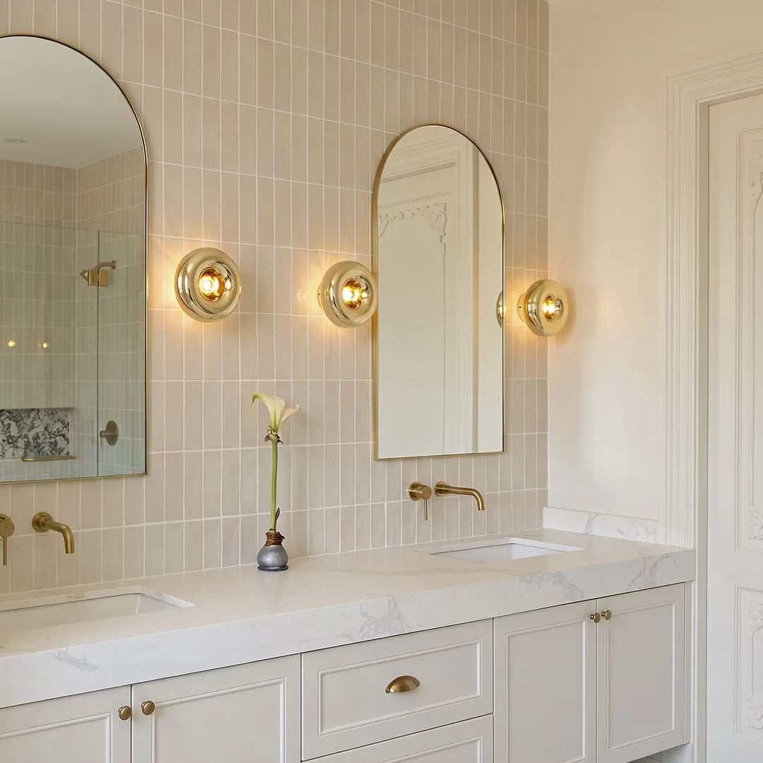 Modern chrome wall sconces flanking arched mirrors above a white double vanity bathroom.