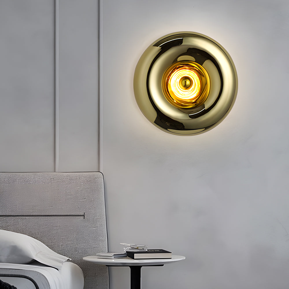 Modern chrome wall sconce with a golden interior, mounted beside a bed.