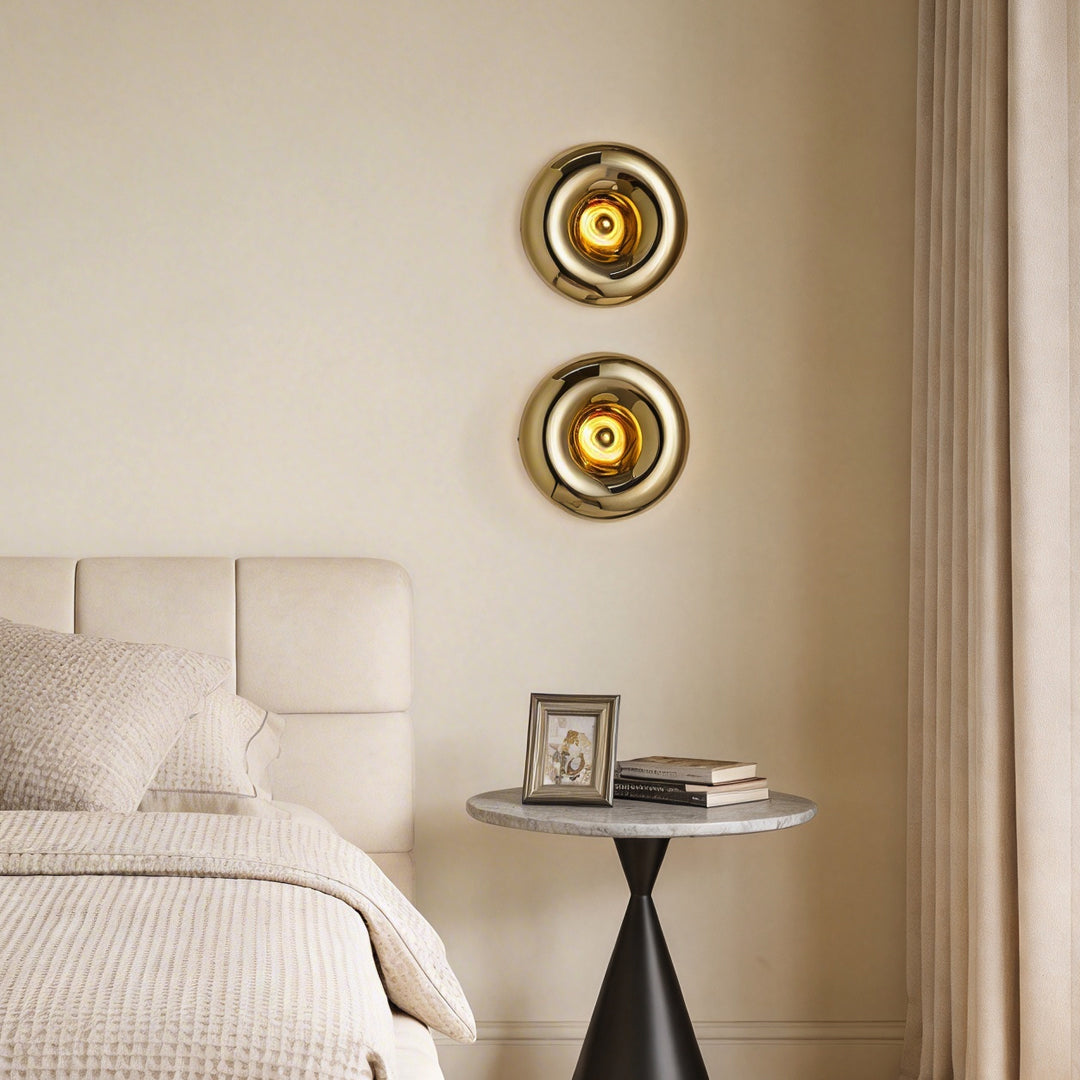 Modern chrome wall sconce with a golden interior, illuminating a stylish bedroom.