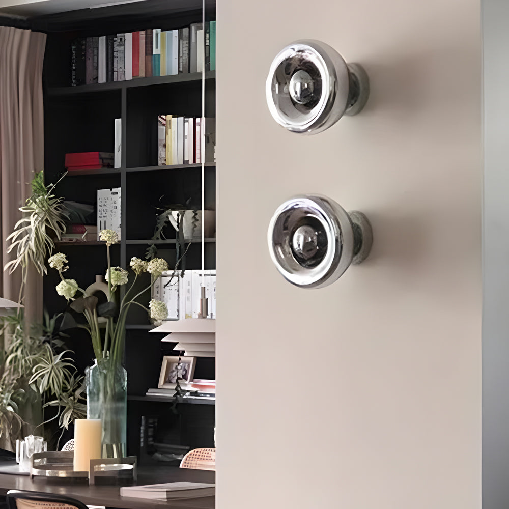 Modern chrome wall sconce with a round design, mounted in a stylish bedroom.