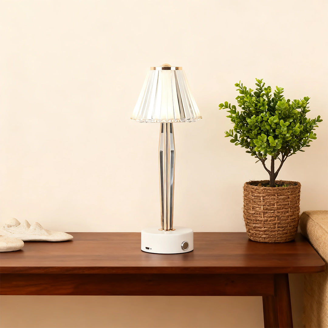 Modern classic table lamp with a pleated crystal shade and gold stem, accenting a wooden console table.