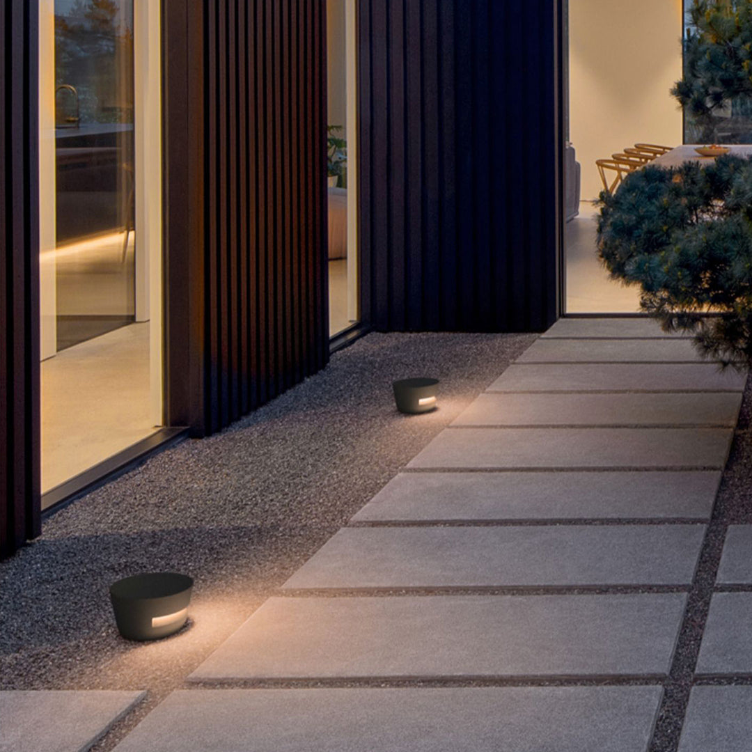 Pair of modern black pathway lights with a concrete-style finish, defining the edge of a paved walkway leading to an entryway.
