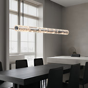 Modern crystal light pendants with a cylindrical design, suspended above a dining table in a bright room.
