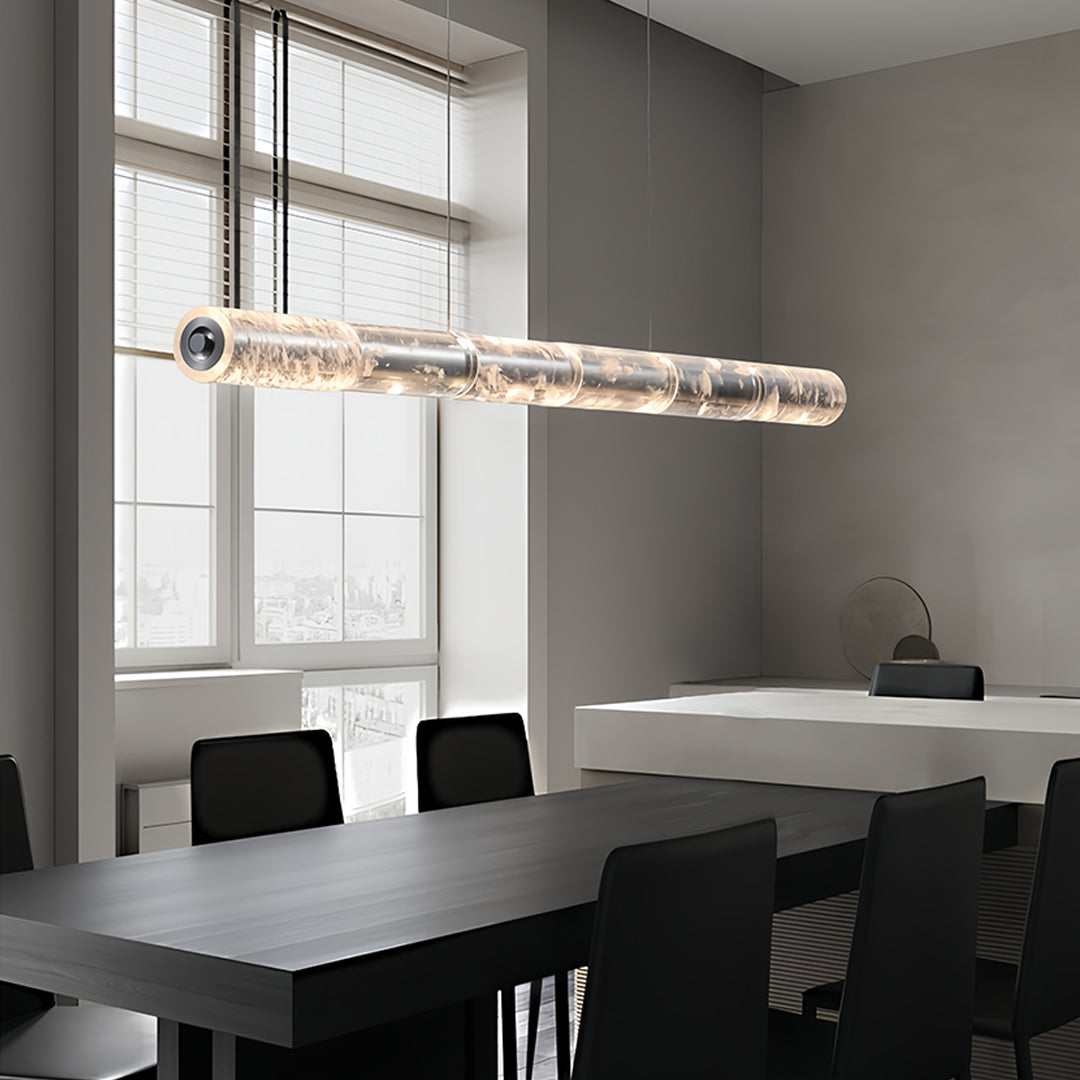 Modern crystal light pendants with a cylindrical design, suspended above a dining table in a bright room.