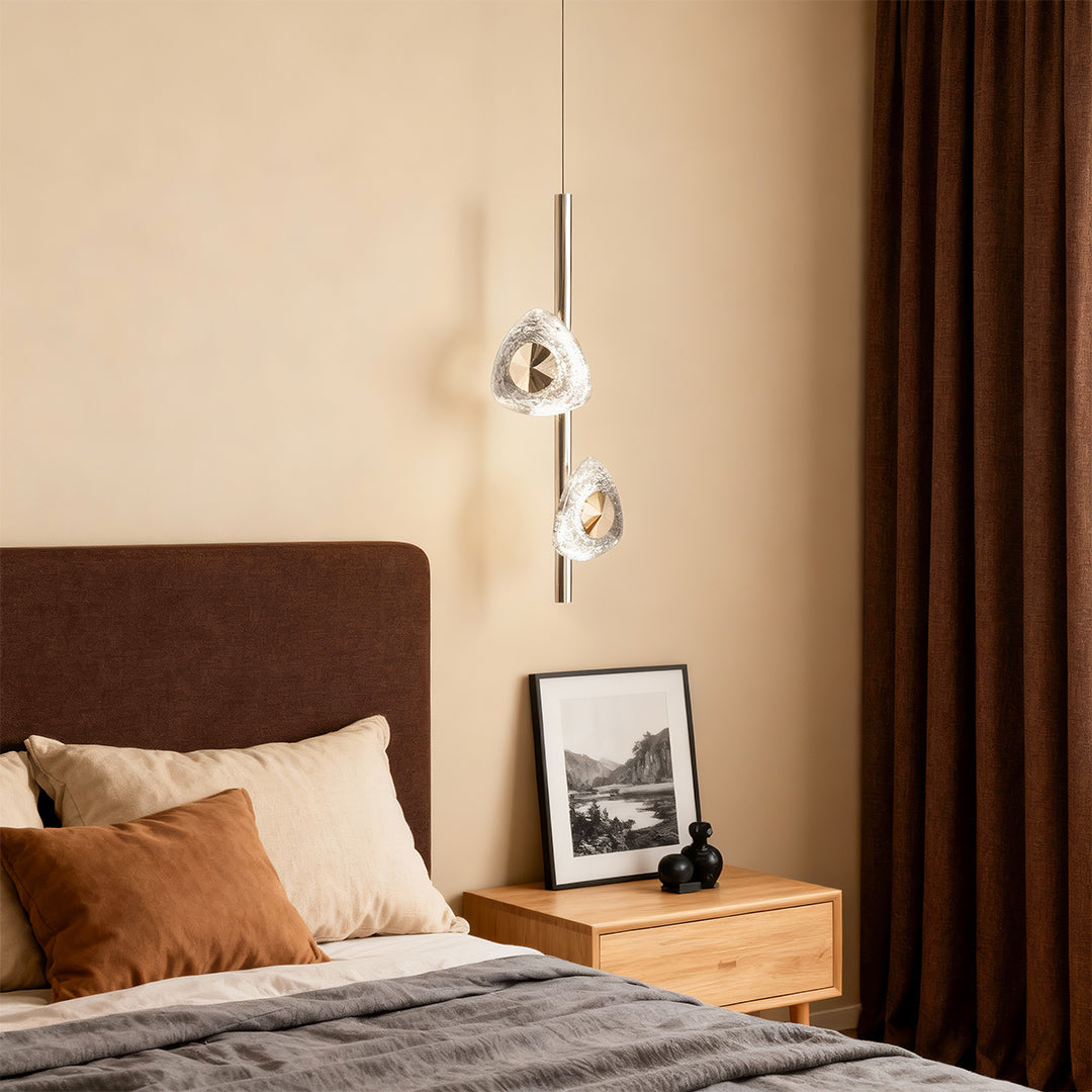 Modern crystal pendant light illuminating bedroom beside brown upholstered headboard with warm ambient glow