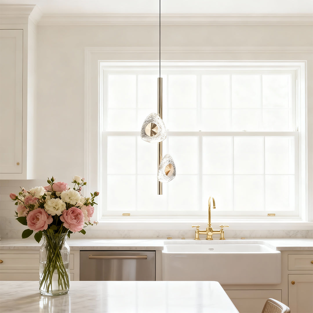 Modern crystal pendant light providing accent lighting in bright kitchen with white cabinetry and natural light