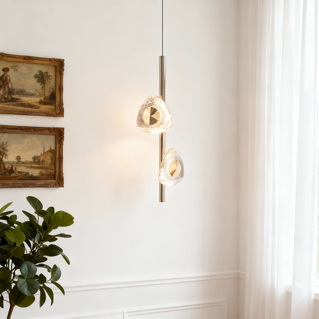 Modern crystal pendant light creating elegant focal point on white wall beside artwork and botanical accents