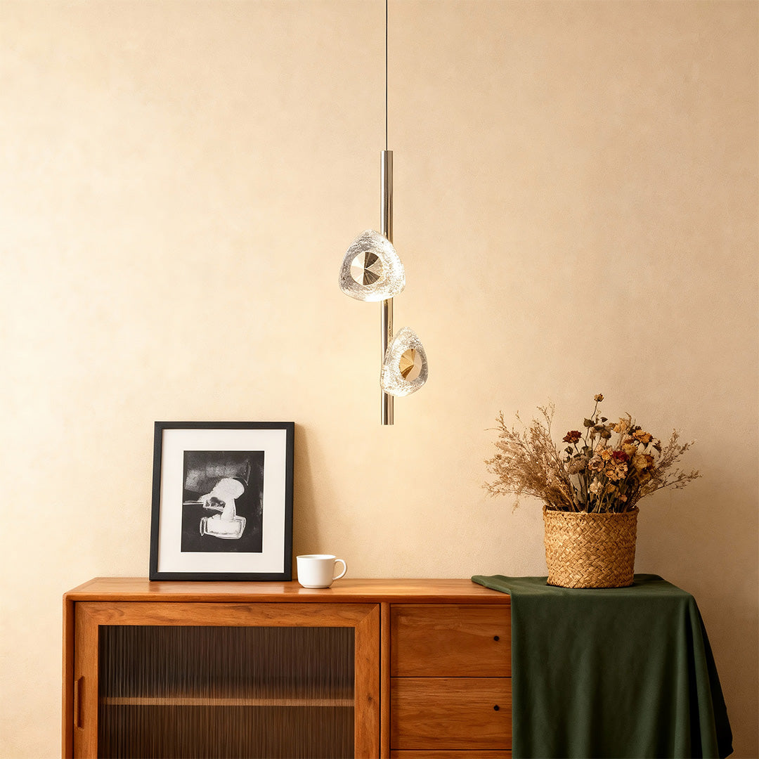 Modern crystal pendant light mounted above wooden credenza with decorative dried flowers in neutral interior