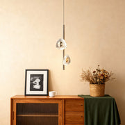 Modern crystal pendant light mounted above wooden credenza with decorative dried flowers in neutral interior