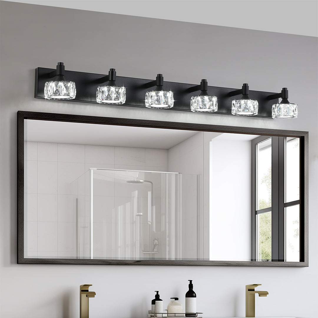 Modern crystal bathroom vanity light with glass shade chandelier design illuminating black-framed mirror in minimalist white bathroom.