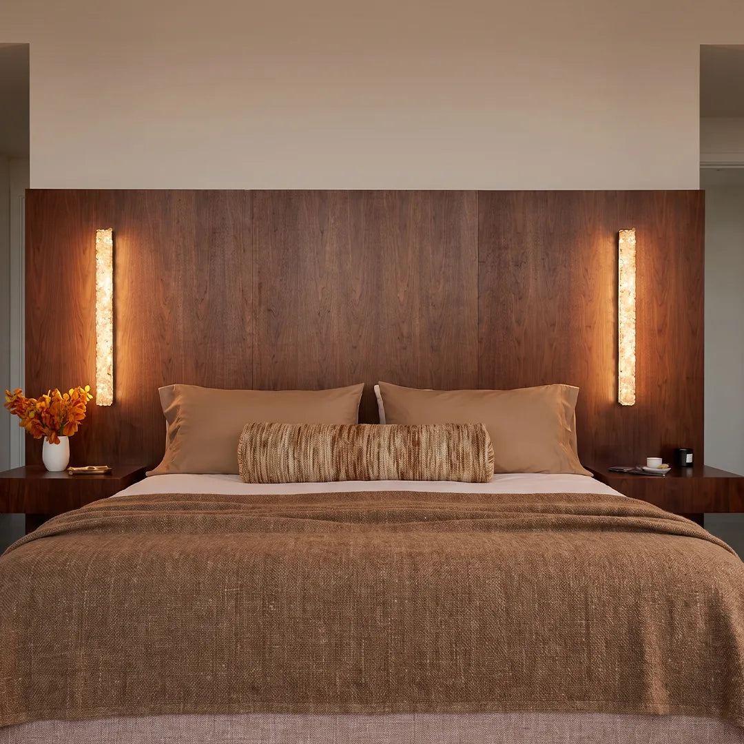 Modern crystal wall lights mounted above a bed against a warm wood accent wall.