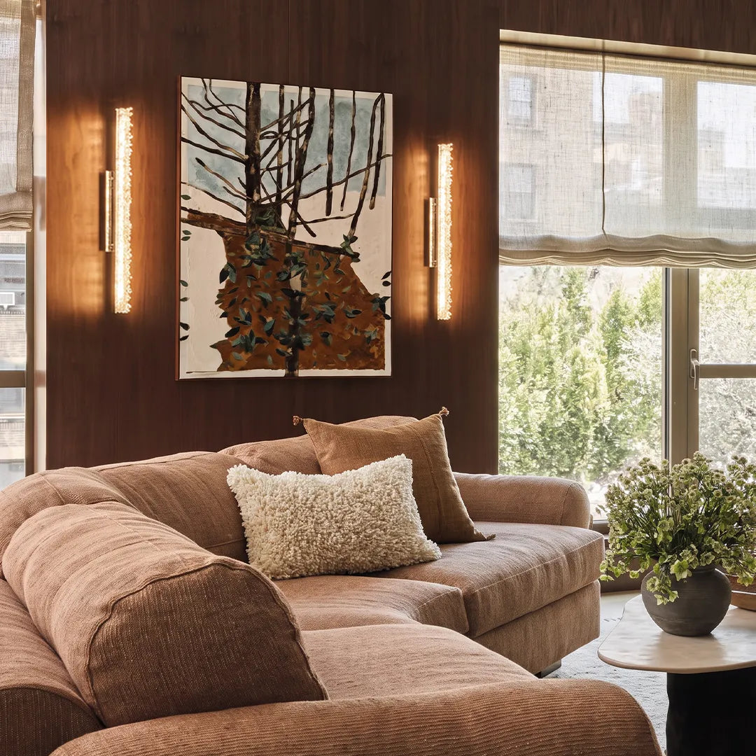 Modern crystal wall lights illuminating a cozy living room beside artwork and a large window.