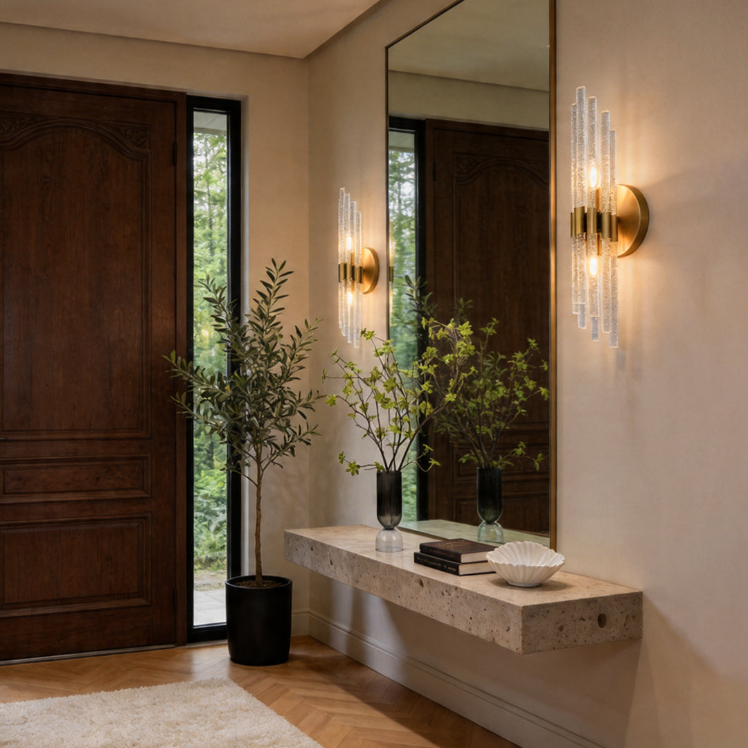 Modern crystal wall lights reflecting in a large mirror above a stone console in an entrance.