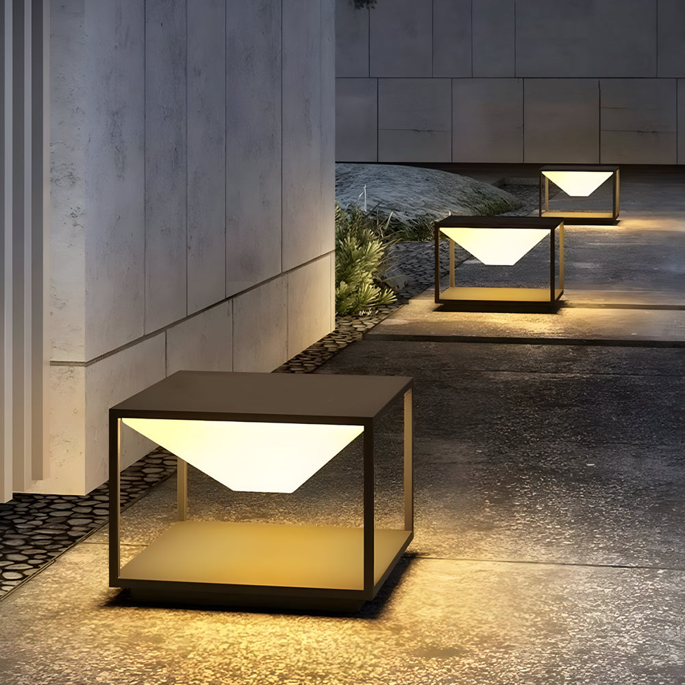 Modern solar pillar light with sleek cubic design creating warm ambient lighting on contemporary outdoor concrete patio