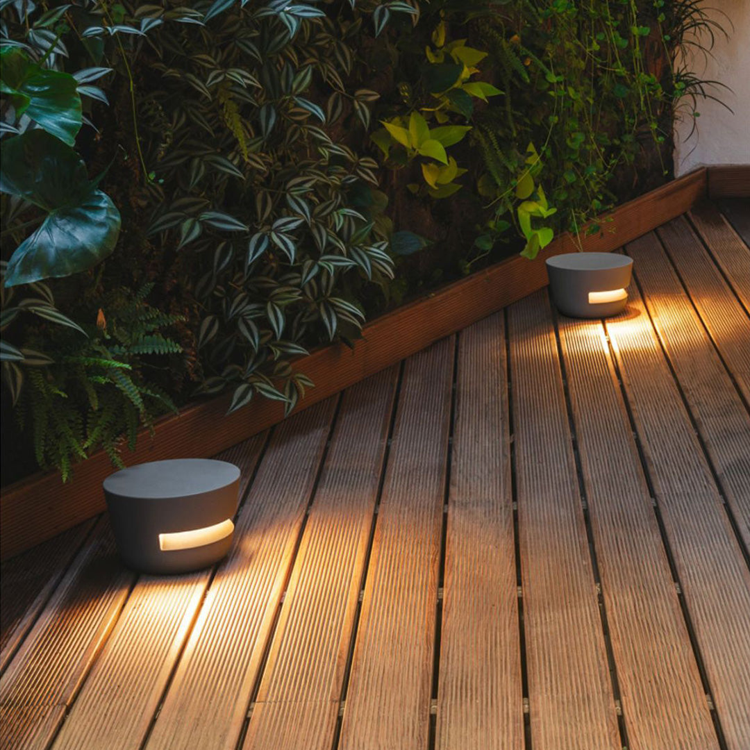 Modern cylindrical black pathway lights embedded in wood decking, casting a warm horizontal glow for safe foot traffic.
