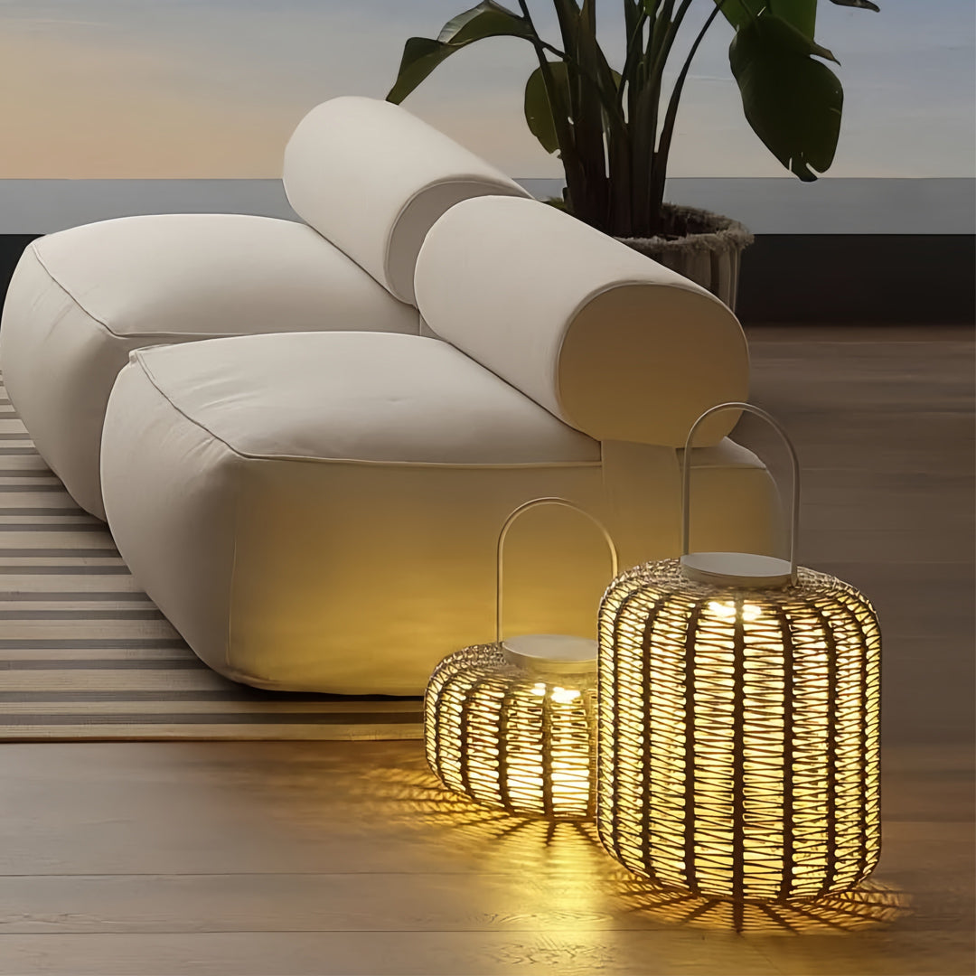 Modern outdoor LED lantern lights with dark woven bases, illuminating a minimalist white modular sofa and large potted plant.