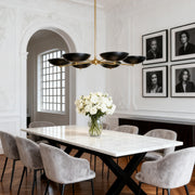 Modern disc black and gold chandeliers with five lights, suspended over a marble-top dining table in a formal room with historical details.