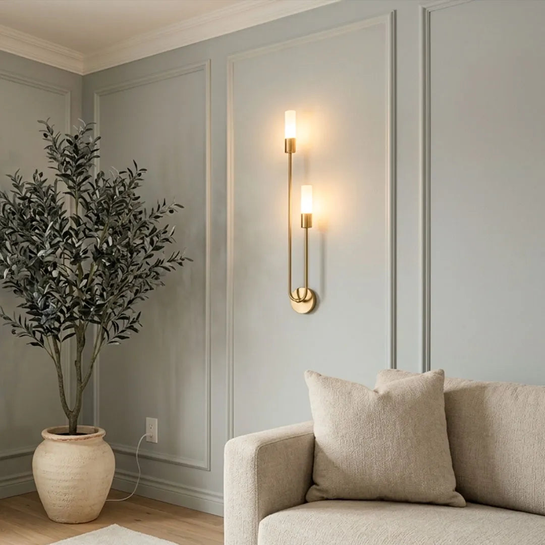 Modern double heads wall sconce mounted on a paneled living room wall, featuring two vertically aligned lights and a brushed gold finish.
