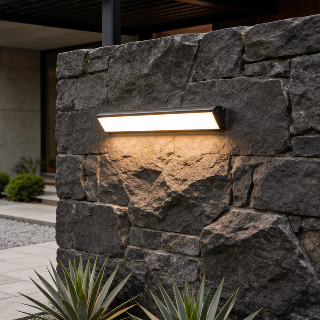 Modern exterior LED wall sconce mounted on a stone wall, providing warm architectural outdoor lighting.