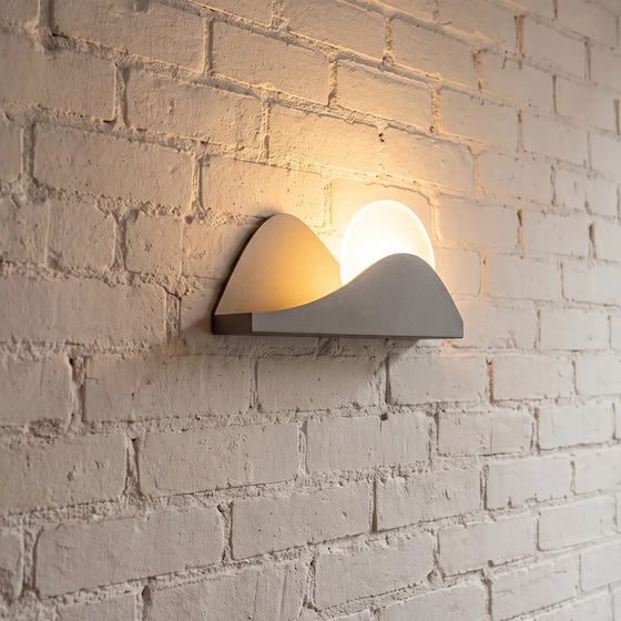Modern exterior wall lighting with a sculptural LED design mounted on a textured brick wall.