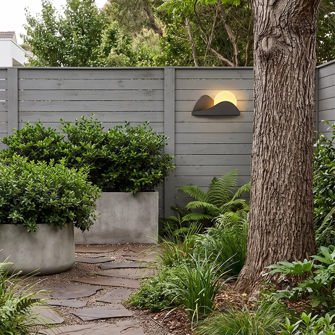 Modern exterior wall lighting installed on a privacy fence surrounded by lush garden landscaping.