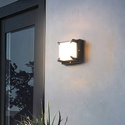 Modern frosted square Black Outdoor Wall Light illuminating a light-colored exterior near a glass door.