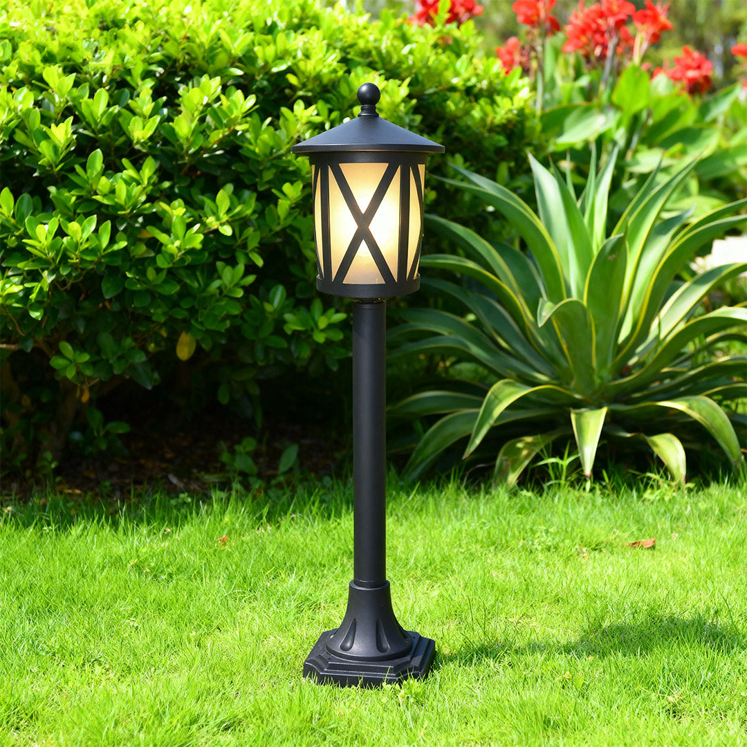 Modern garden bollard light standing on vibrant grass near decorative agave plants in daytime