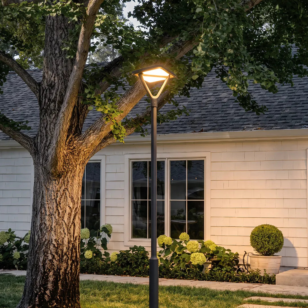Modern garden street light beside a large tree outside a residential home at dusk.