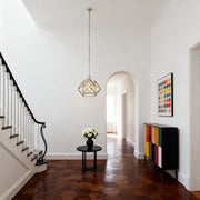 Modern geometric gold metal pendant light with an open cage design, suspended in a bright, high-ceiling entryway or foyer.