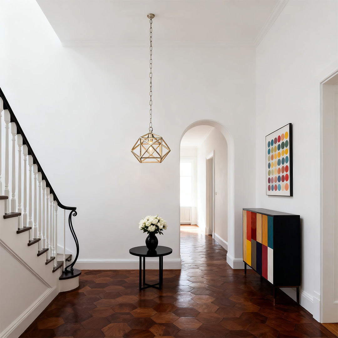 Modern geometric gold metal pendant light with an open cage design, suspended in a bright, high-ceiling entryway or foyer.