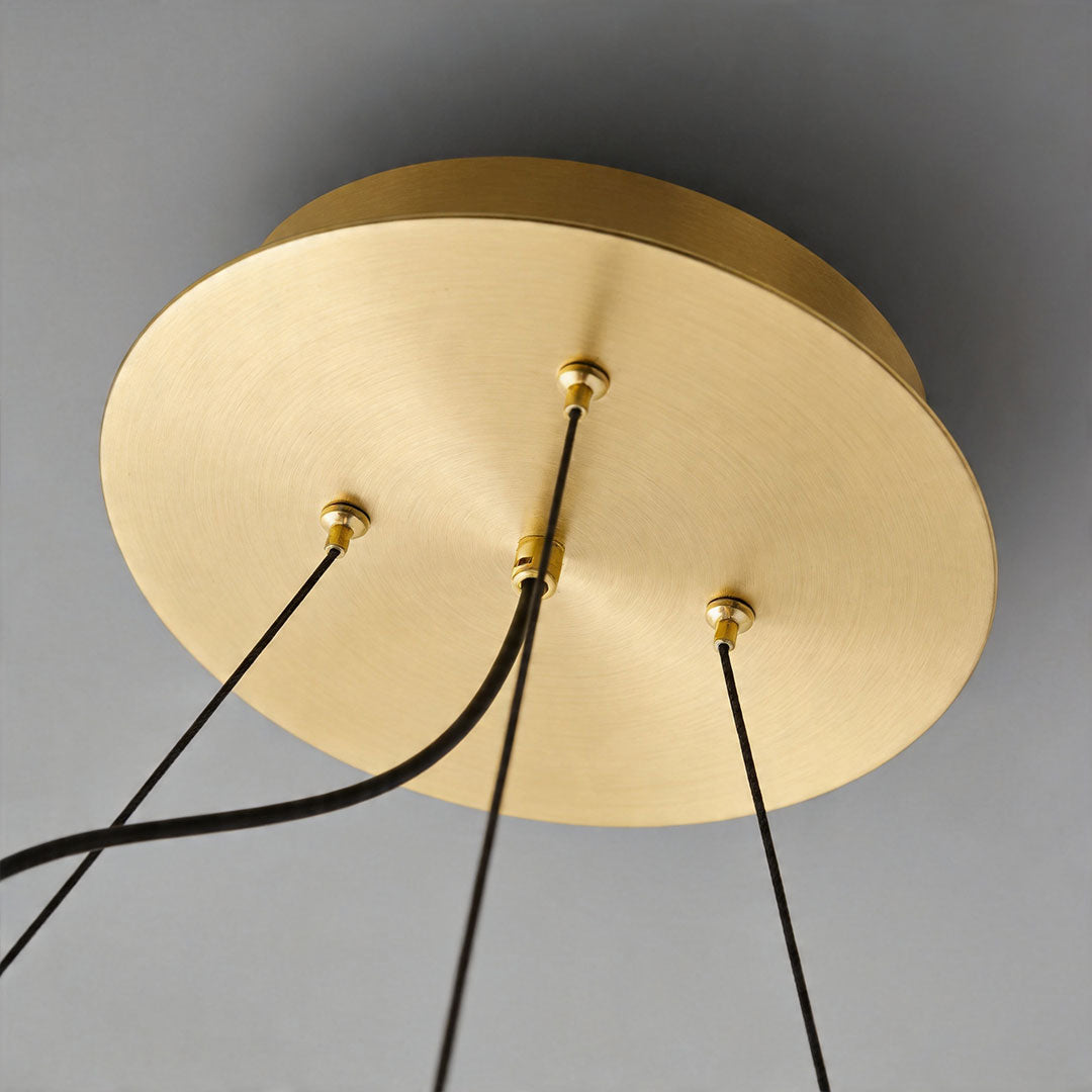 Ceiling canopy detail of modern glam chandelier with brushed gold finish and multiple suspension wires.