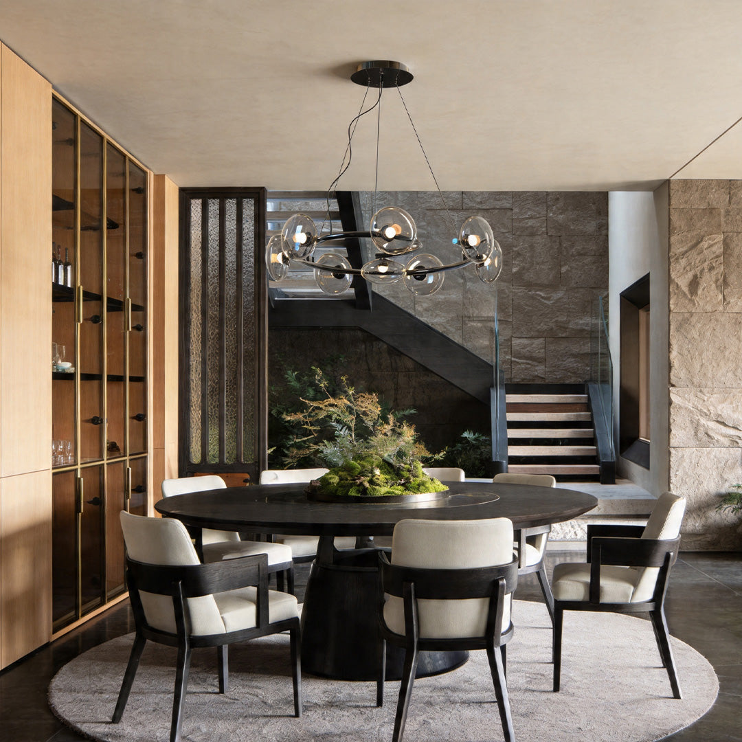 Contemporary glam chandelier installed above a dining table in a modern interior with wood and stone accents.