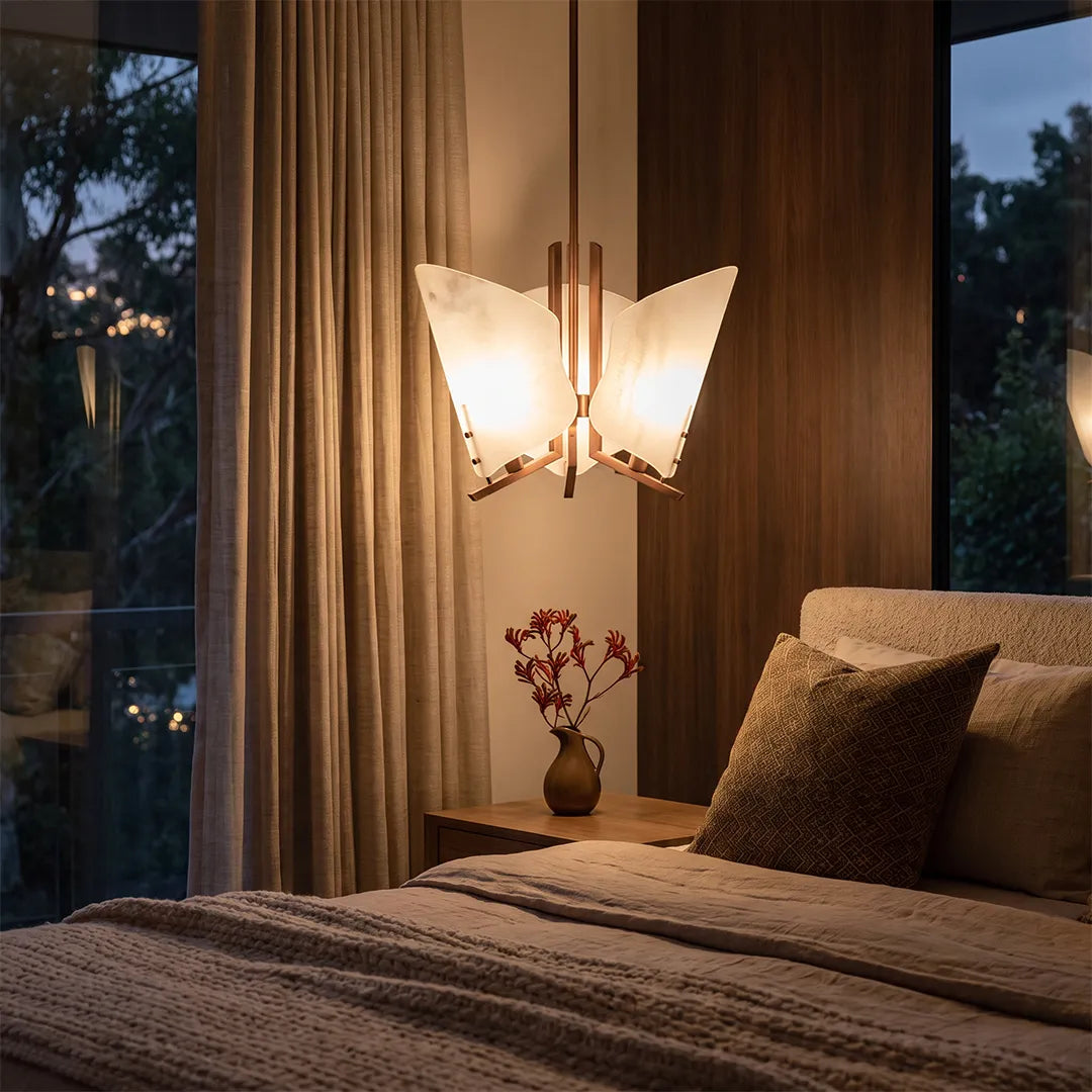 Modern glass chandelier beside a bed in a cozy bedroom with floor-to-ceiling curtains.