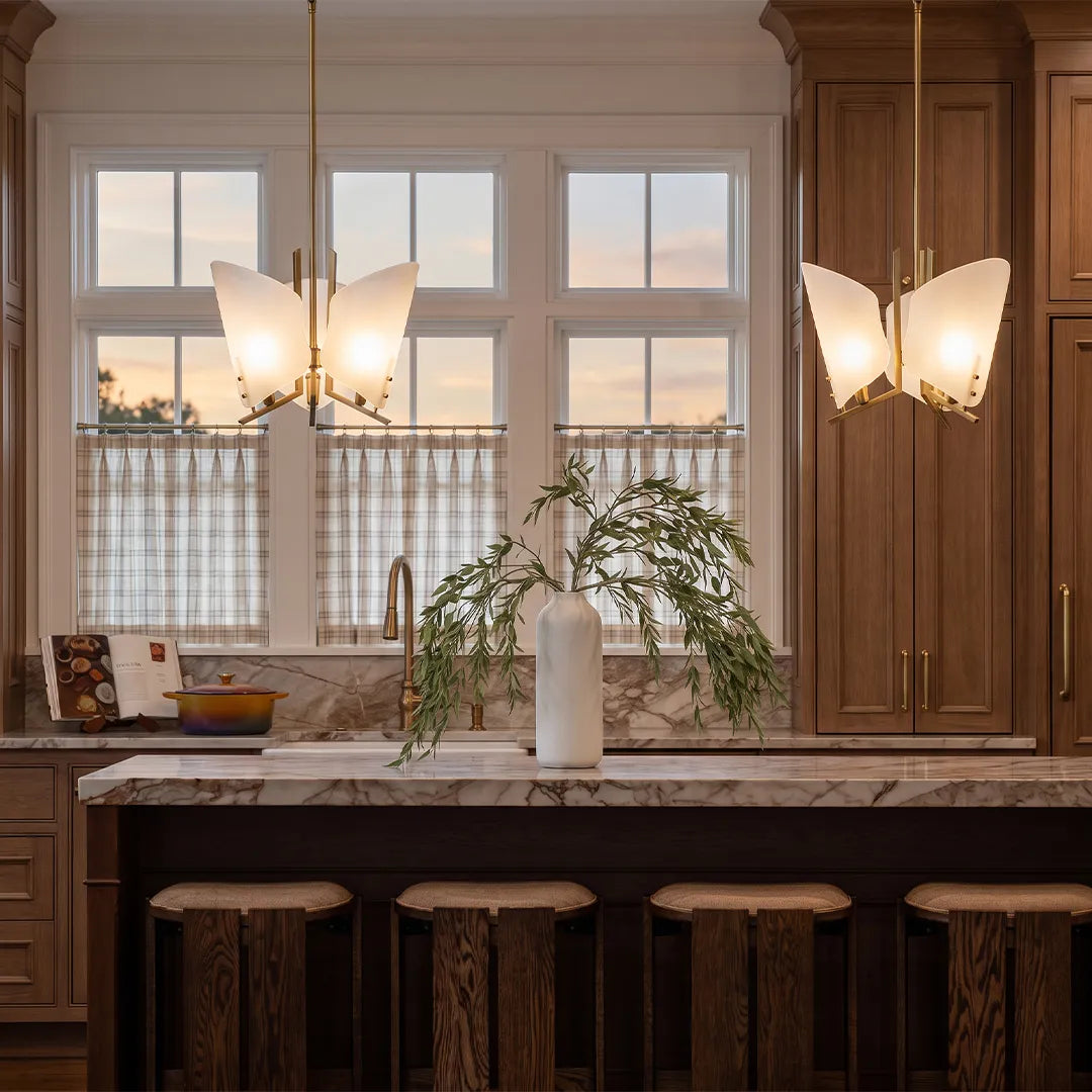 Modern glass chandelier installed above a kitchen island with wood cabinetry and marble countertops.
