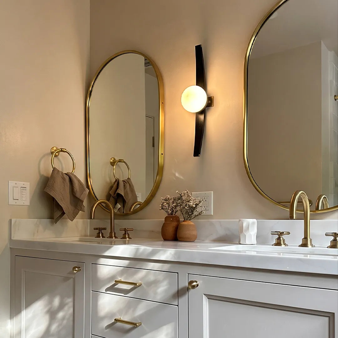 Modern globe wall sconce mounted beside a bathroom mirror with a black curved frame and glowing glass globe.