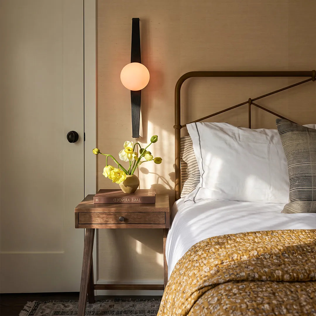Modern globe wall sconce installed above a bedside table with a warm glowing globe and black vertical frame.
