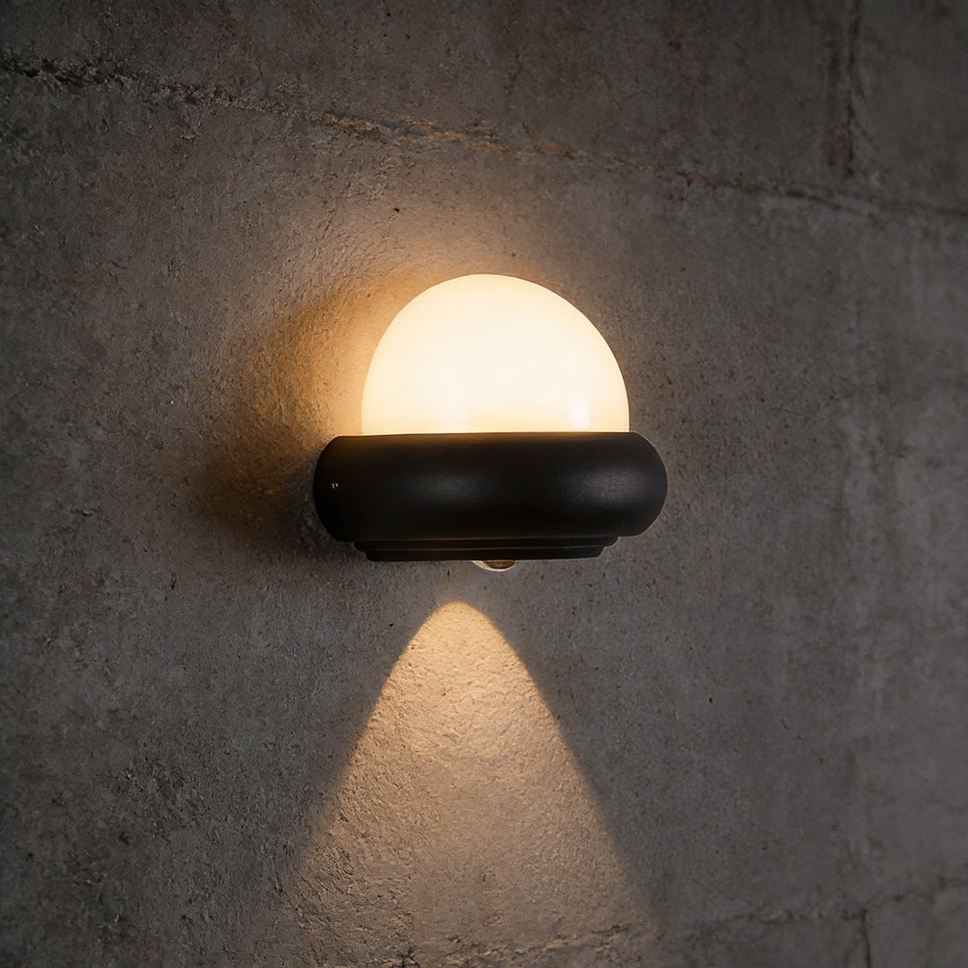 Modern globe wall sconce in black, mounted on a concrete wall for stylish outdoor lighting.