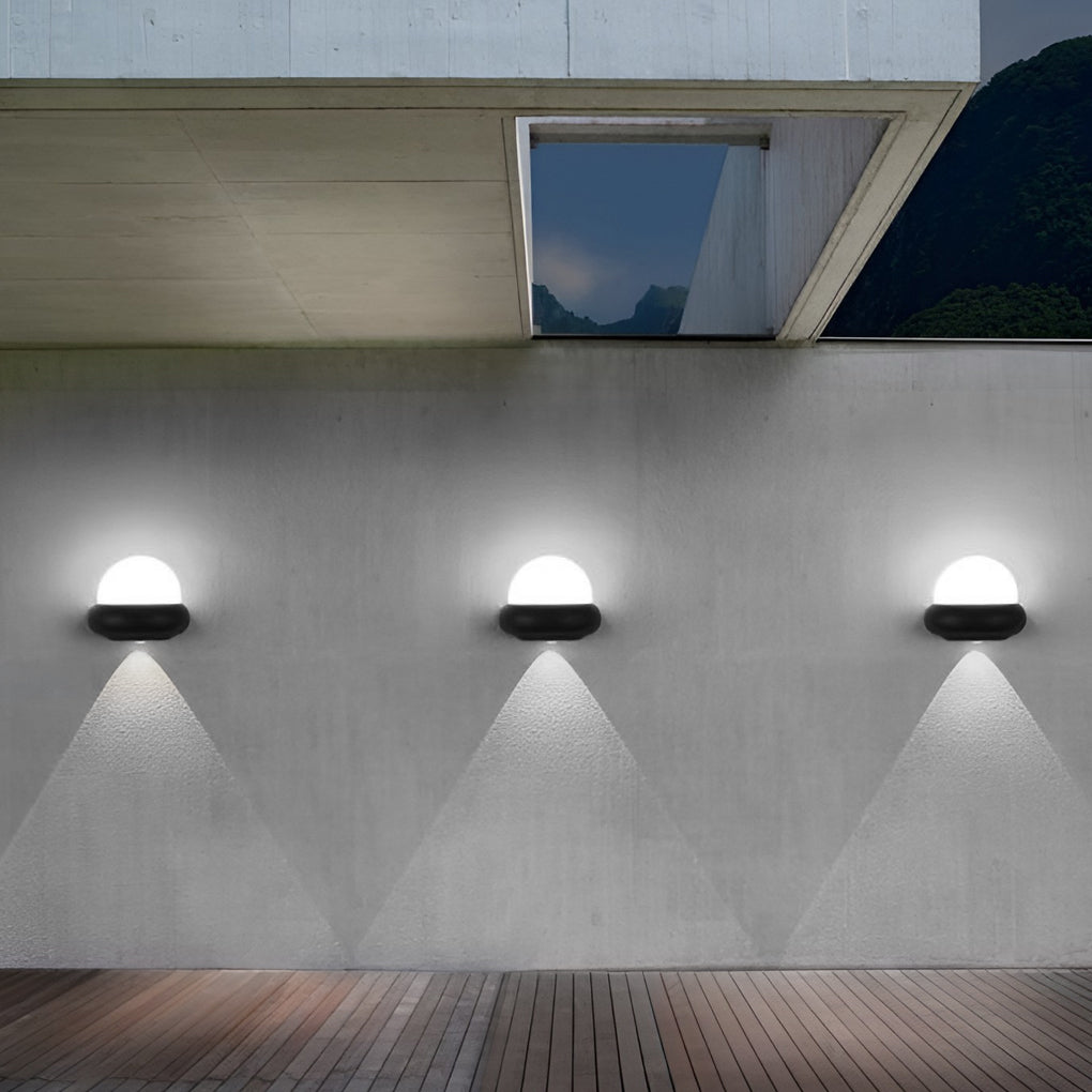 Modern globe wall sconce with black finish, casting soft light in a modern outdoor setting.