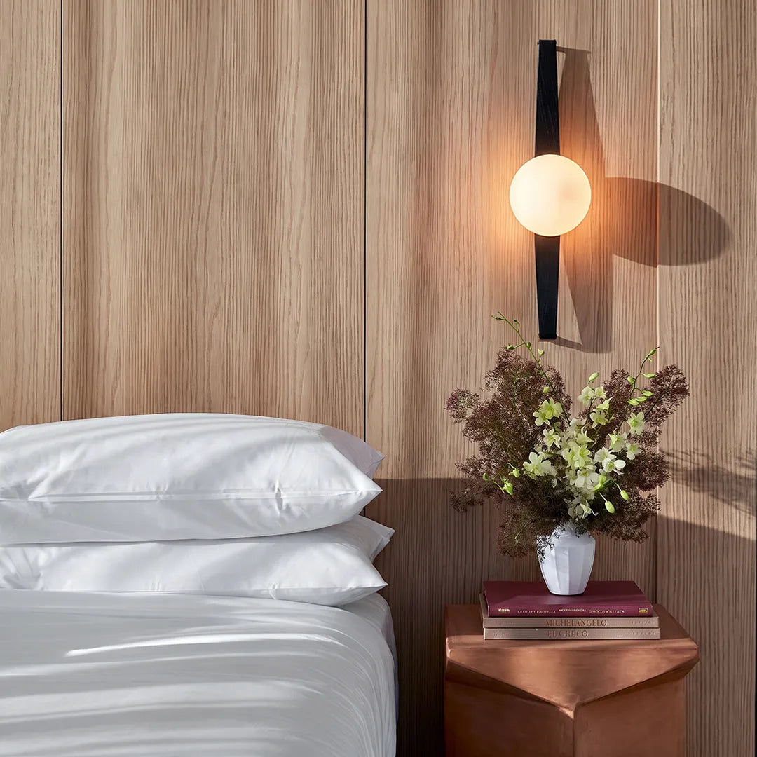 Modern globe wall sconce styled above a bedside table against a wood panel wall with a glowing globe shade.