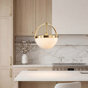 Modern gold and white pendant light with a brass arch and frosted bowl over a kitchen island.