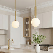 Modern gold hanging lights with frosted glass globes over a bright marble kitchen island desk.