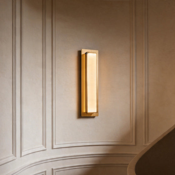 Modern gold wall light fixture glowing on a classic curved paneled wall in a luxury home space.