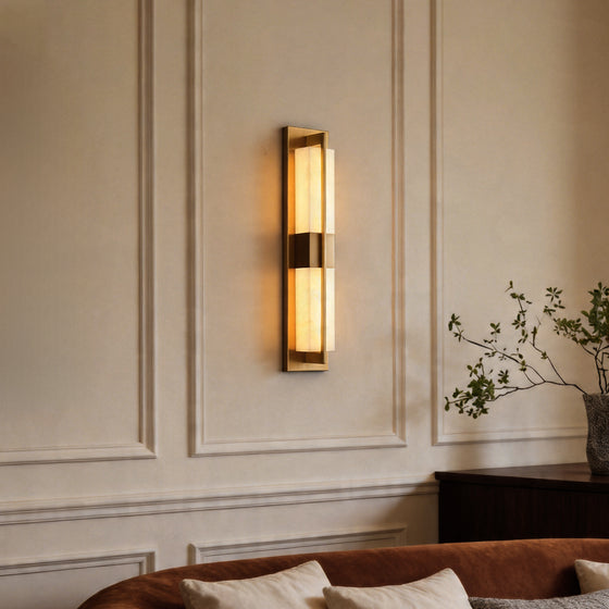 Modern gold wall lighting fixture glowing on a classic paneled wall above a brown sofa set.