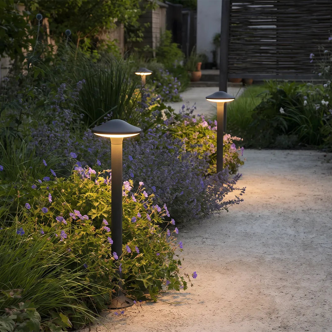 Modern gray mushroom path lights illuminating a curved walkway through a flowering garden