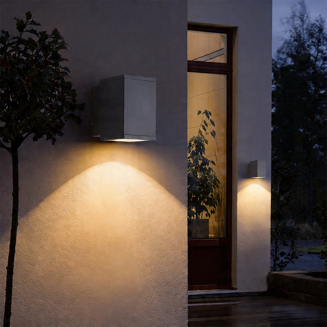 Modern grey wall sconce up and down light illuminating a textured outdoor stucco wall at night
